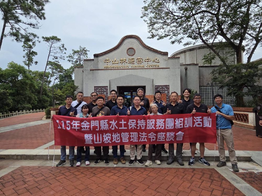 十餘位服務團成員站在中山林遊客中心前合影，前排拉著紅色布條，上面寫著「115年金門縣水土保持服務團組訓活動暨山坡地管理法令座談會」。